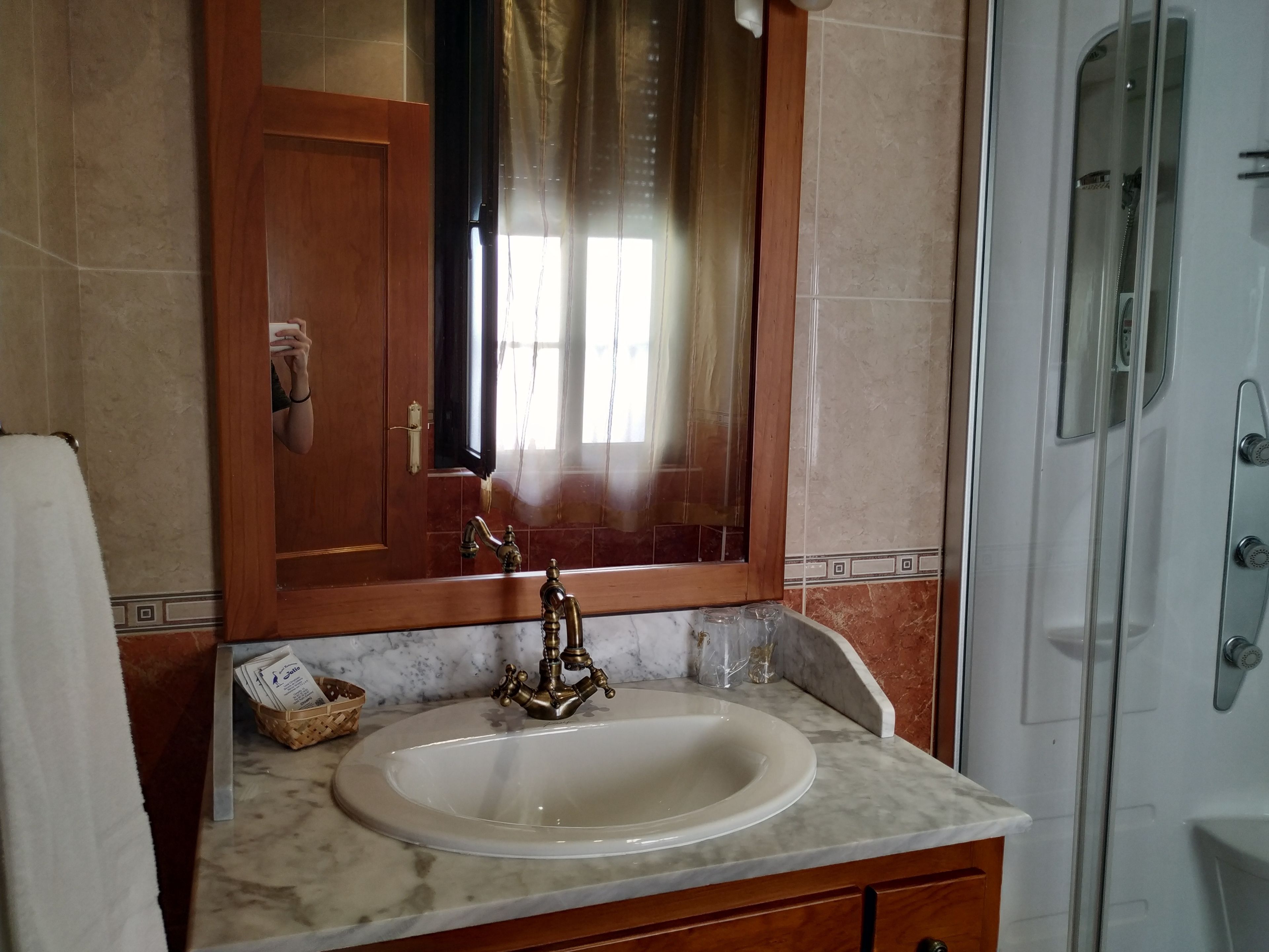 Un bagno con lavabo in marmo, mobile contenitore in legno, specchio e cabina doccia in vetro.