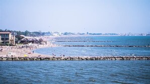 Une plage côtière avec des brise-lames rocheux, une étendue de sable et des bâtiments en arrière-plan.