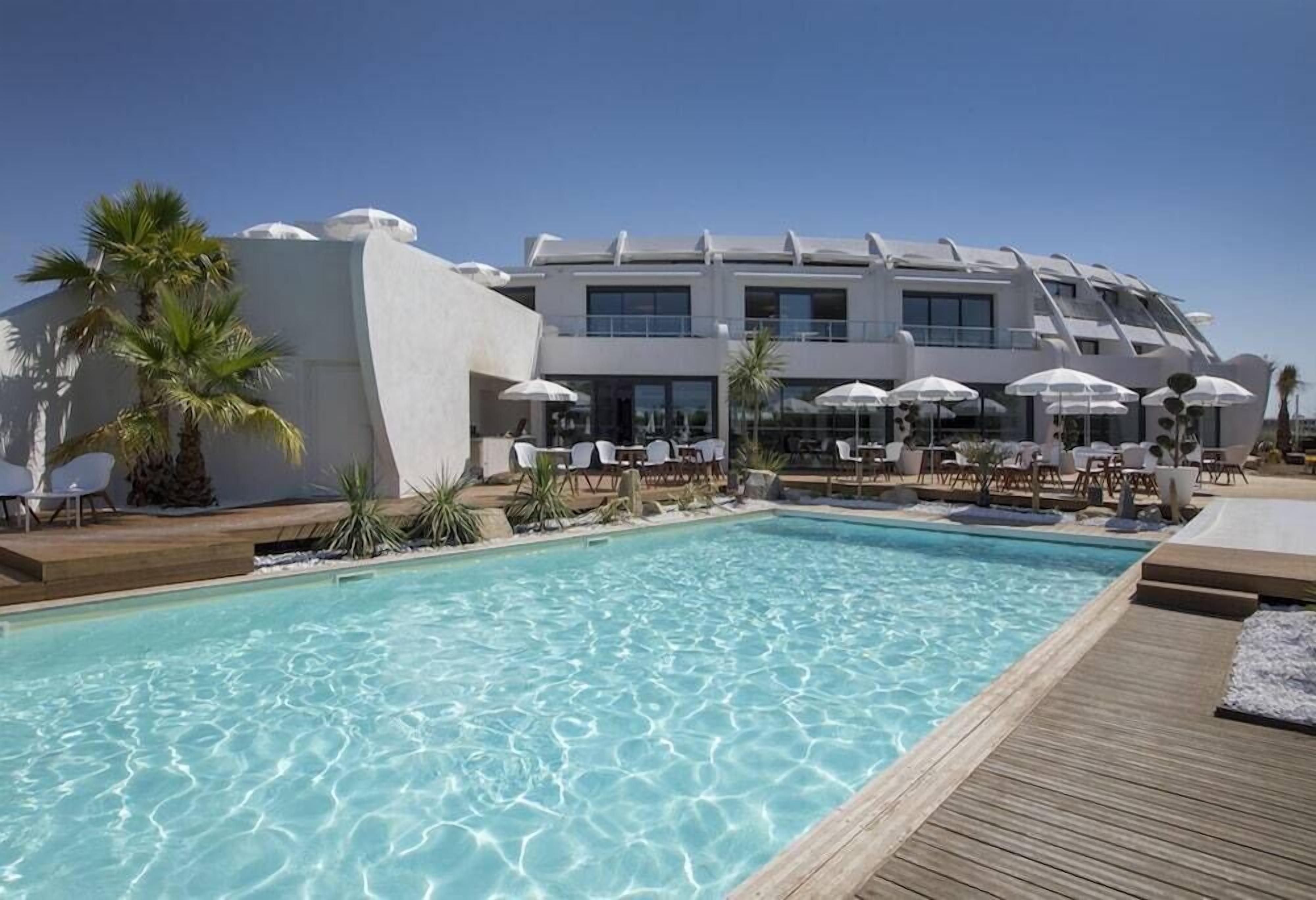 Ein modernes Hotel mit Pool, weißen Sonnenschirmen und Liegestühlen.