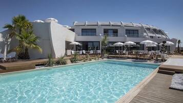 Ein modernes Hotel mit Pool, weißen Sonnenschirmen und Liegestühlen.