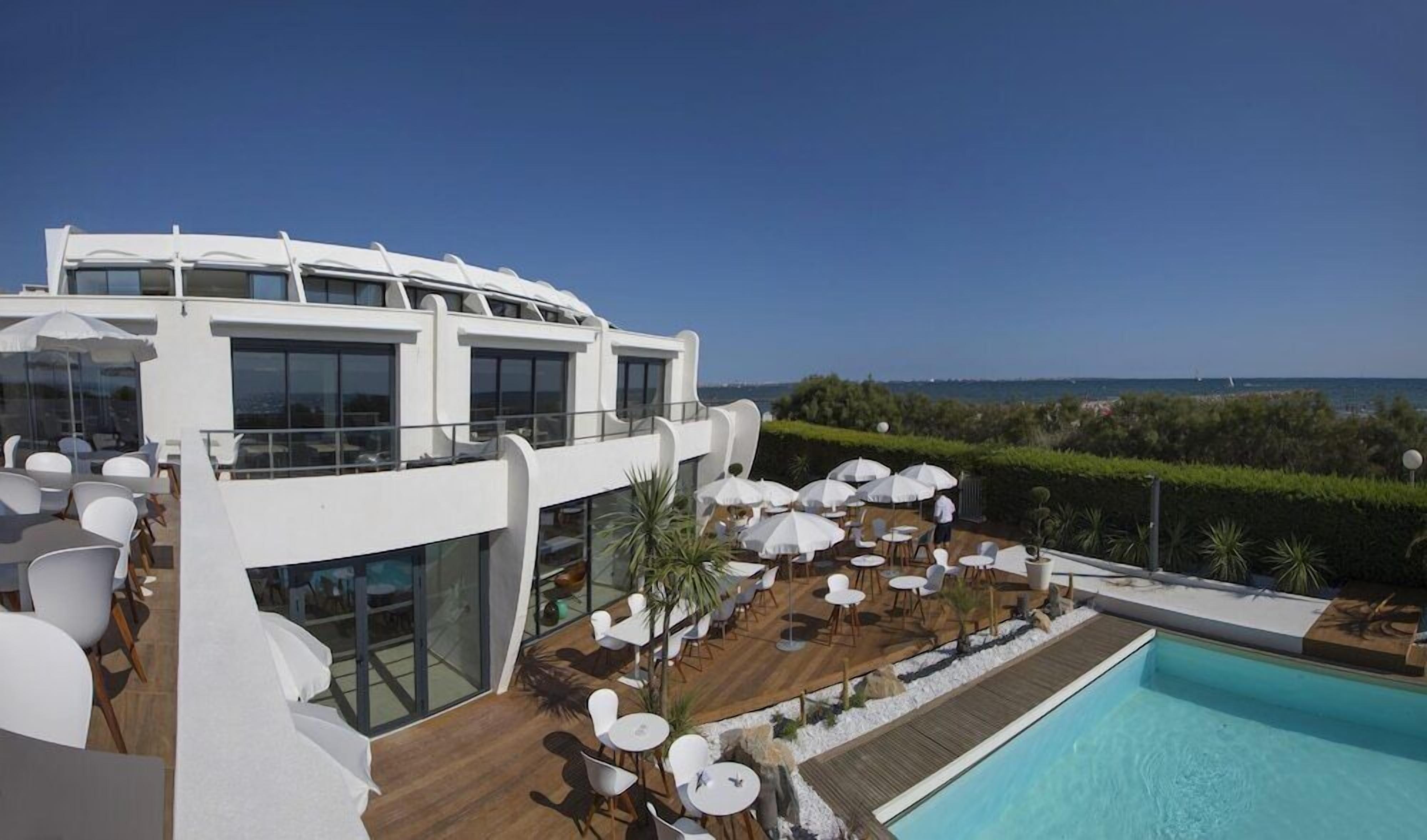 Un espace piscine extérieur moderne, doté de plusieurs coins salon et offrant une vue sur la mer.