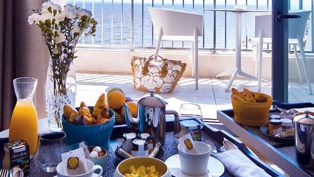 Un plateau de petit-déjeuner installé sur un balcon avec vue sur la mer, comprenant des œufs, des toasts et des fruits.