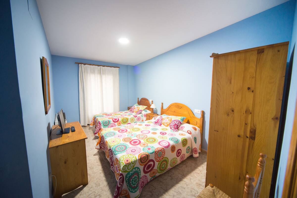 A bedroom with two beds, a wooden desk, and a wardrobe.