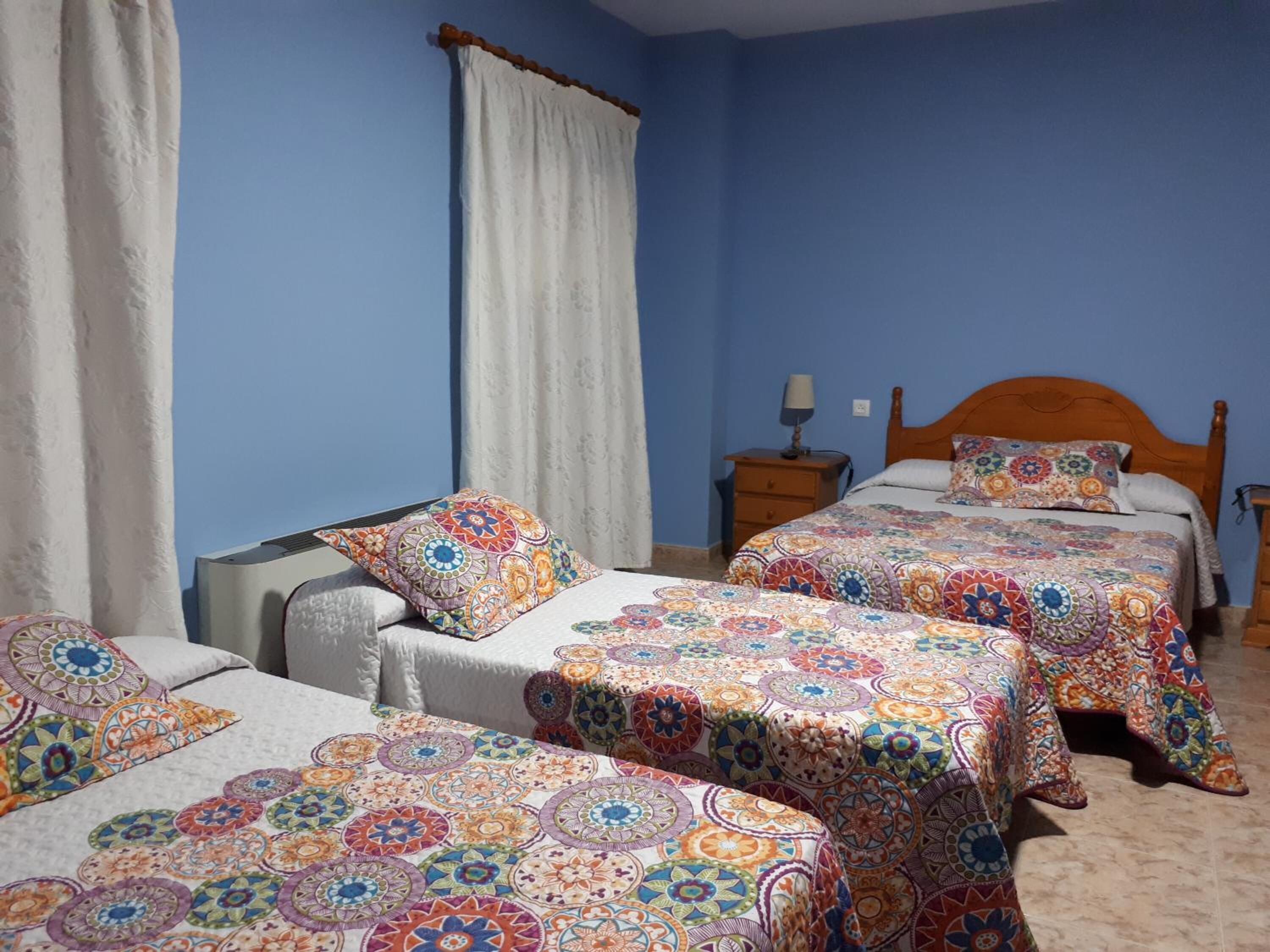 A bedroom with two beds, a nightstand, and a window with curtains.