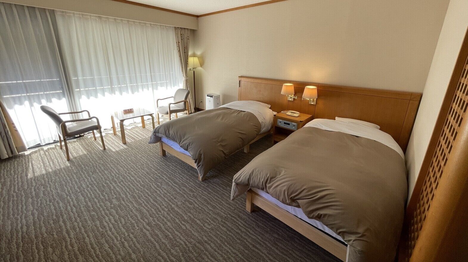 Habitación de hotel con dos camas, un escritorio, una silla, una lámpara y un teléfono en la mesita de noche.