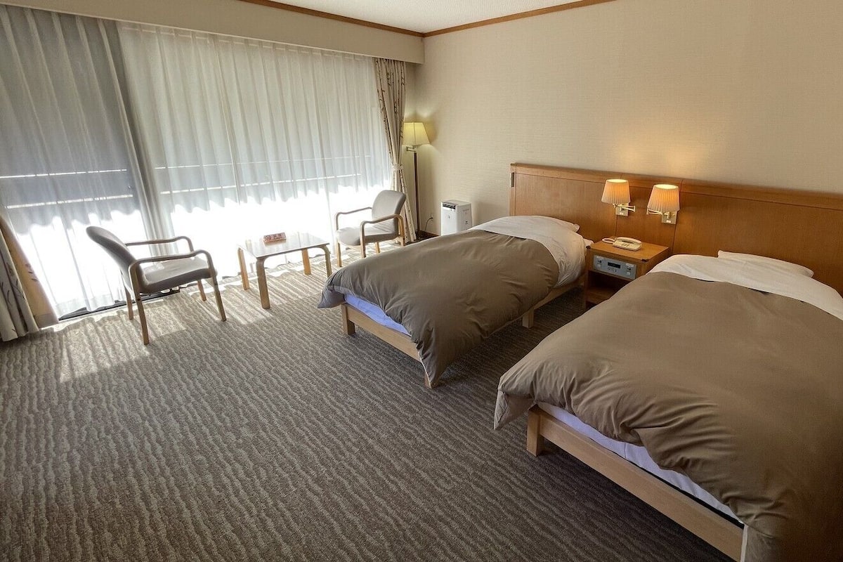 A hotel room with two beds, a desk, a chair, a lamp, and a phone on the nightstand.