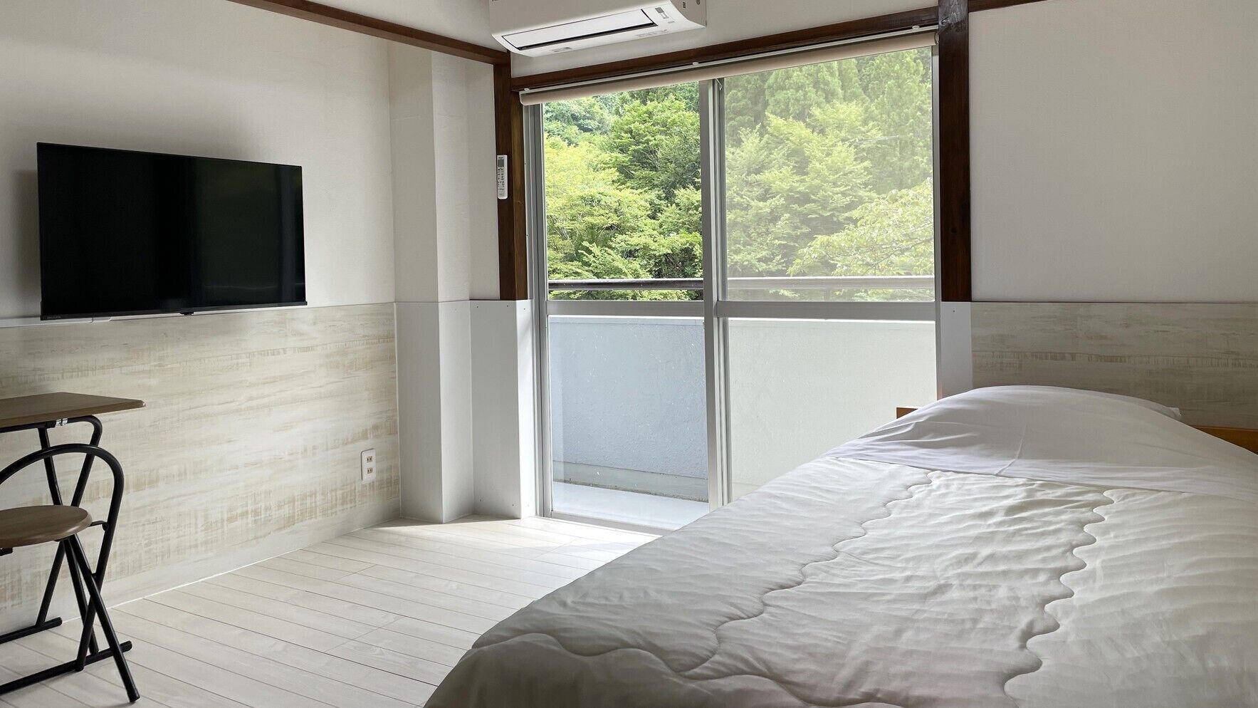 Un dormitorio con cama, televisor, mesa y puerta corrediza de vidrio a un balcón.
