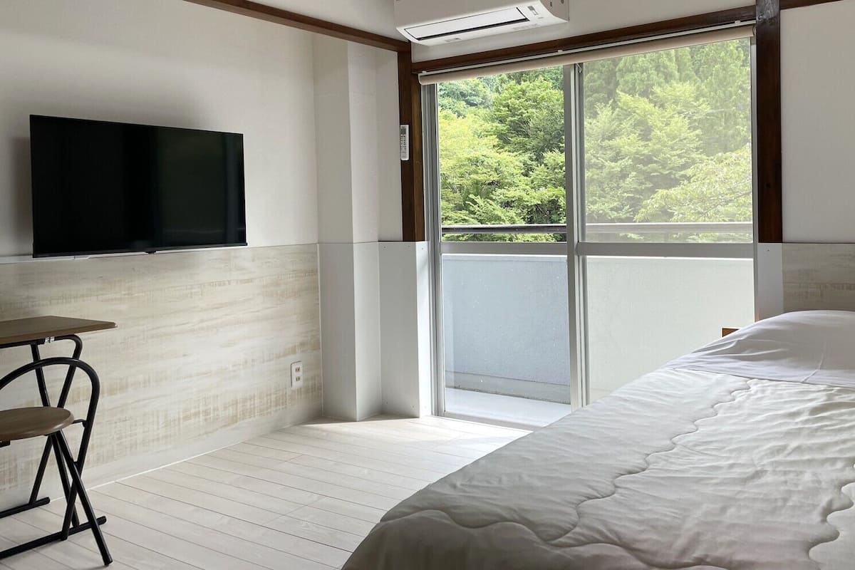 A bedroom with a bed, a TV, a table, and a sliding glass door to a balcony.