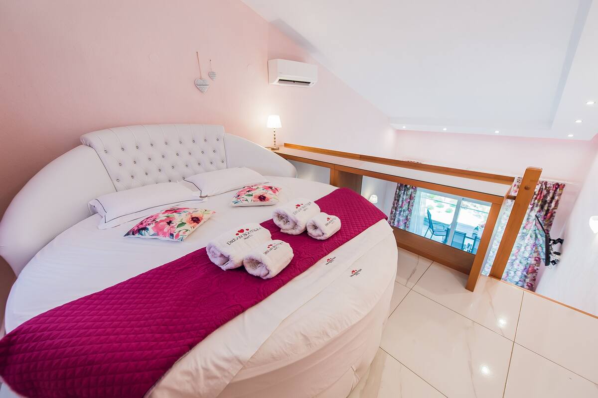 A bedroom with a bed, a red blanket, and towels with text.