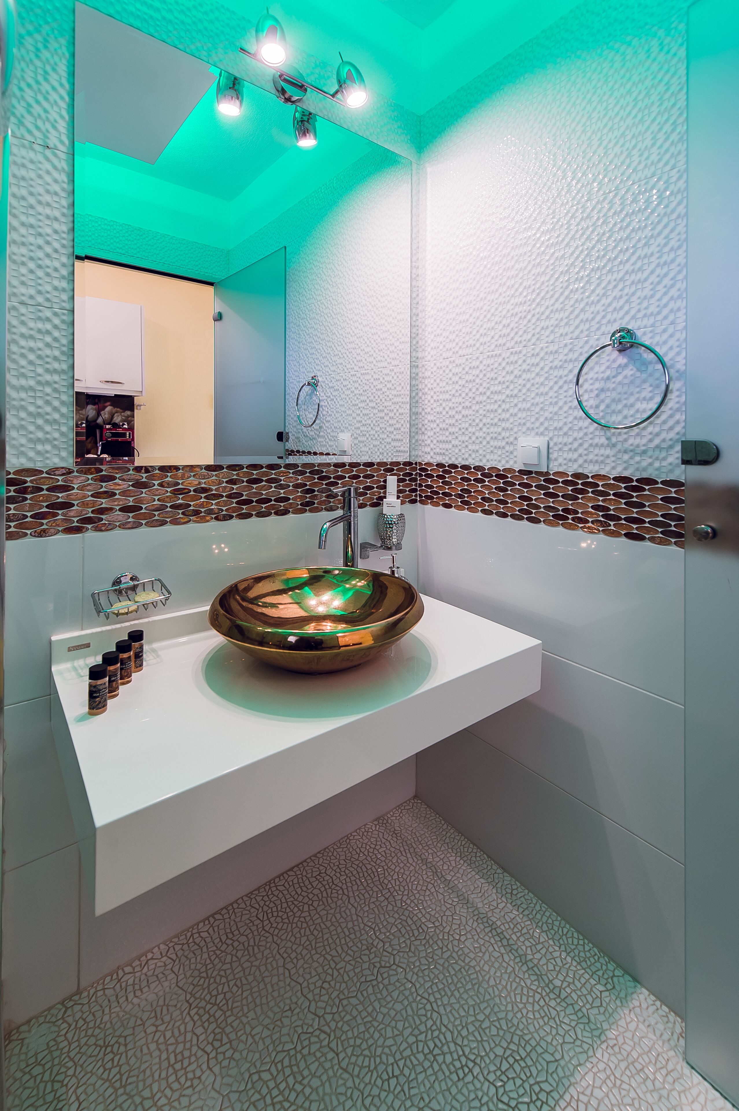 Een moderne badkamer met een grote, ronde, metalen wastafel, een witte wastafelmeubel, een structuurwand en een spiegel boven de wastafel.