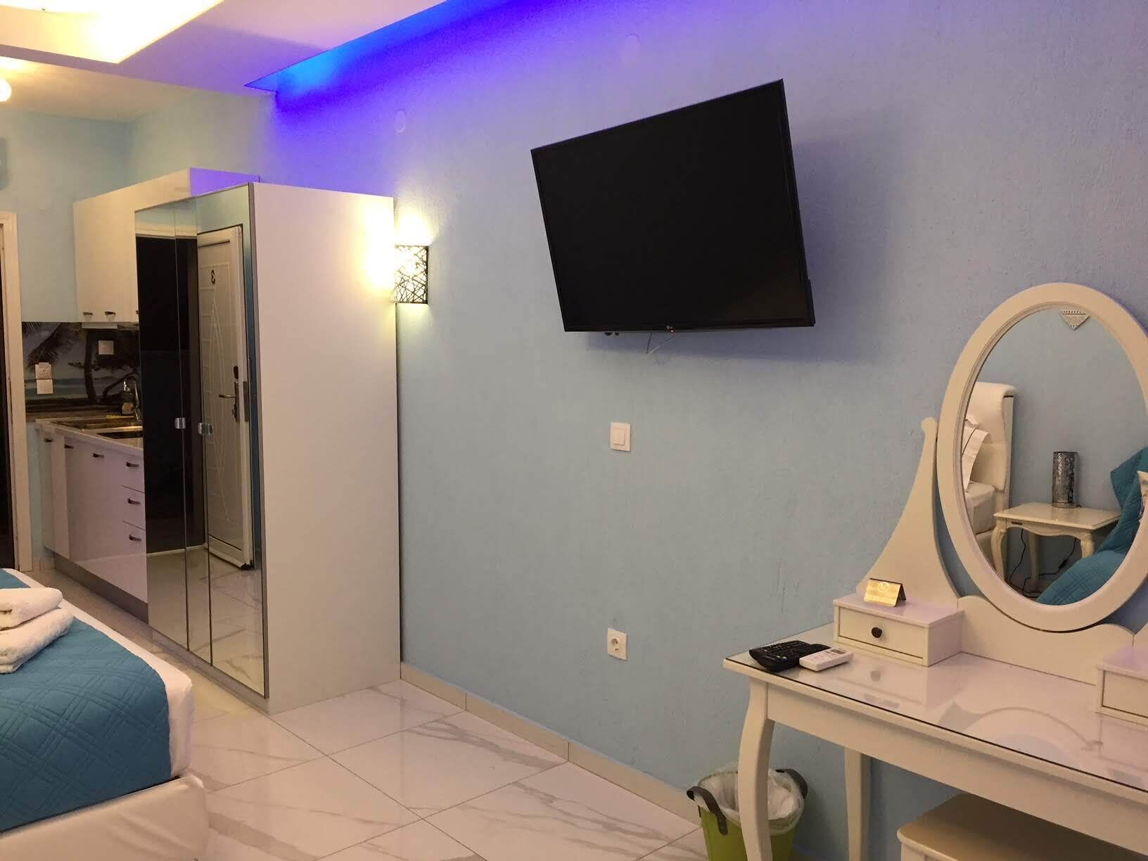 Un dormitorio con cama, escritorio con espejo, televisor y baño con lavabo y espejo.