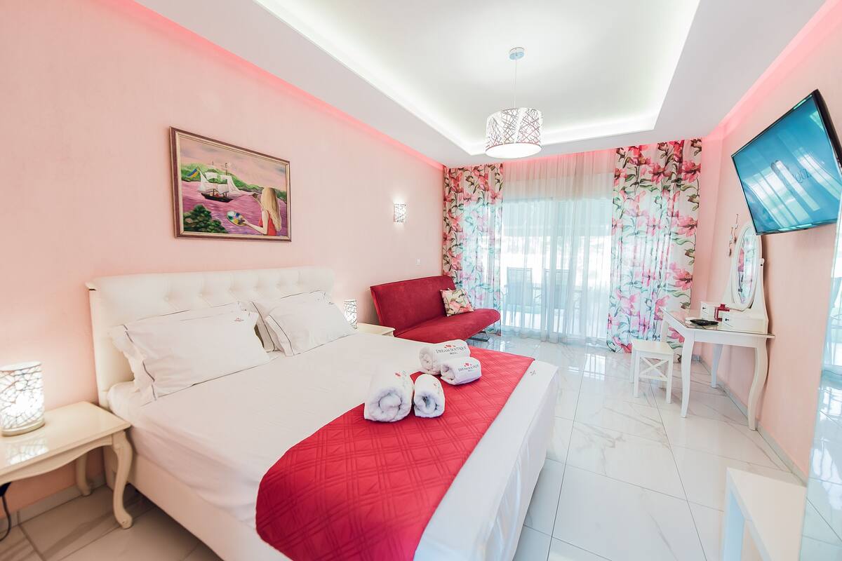 A hotel room with a large bed, a red chair, a desk, and a TV.
