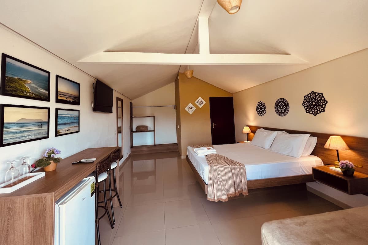 Une chambre d’hôtel comprenant un lit, des tables de chevet, un bureau avec des chaises, une télévision et des œuvres d’art accrochées aux murs.
