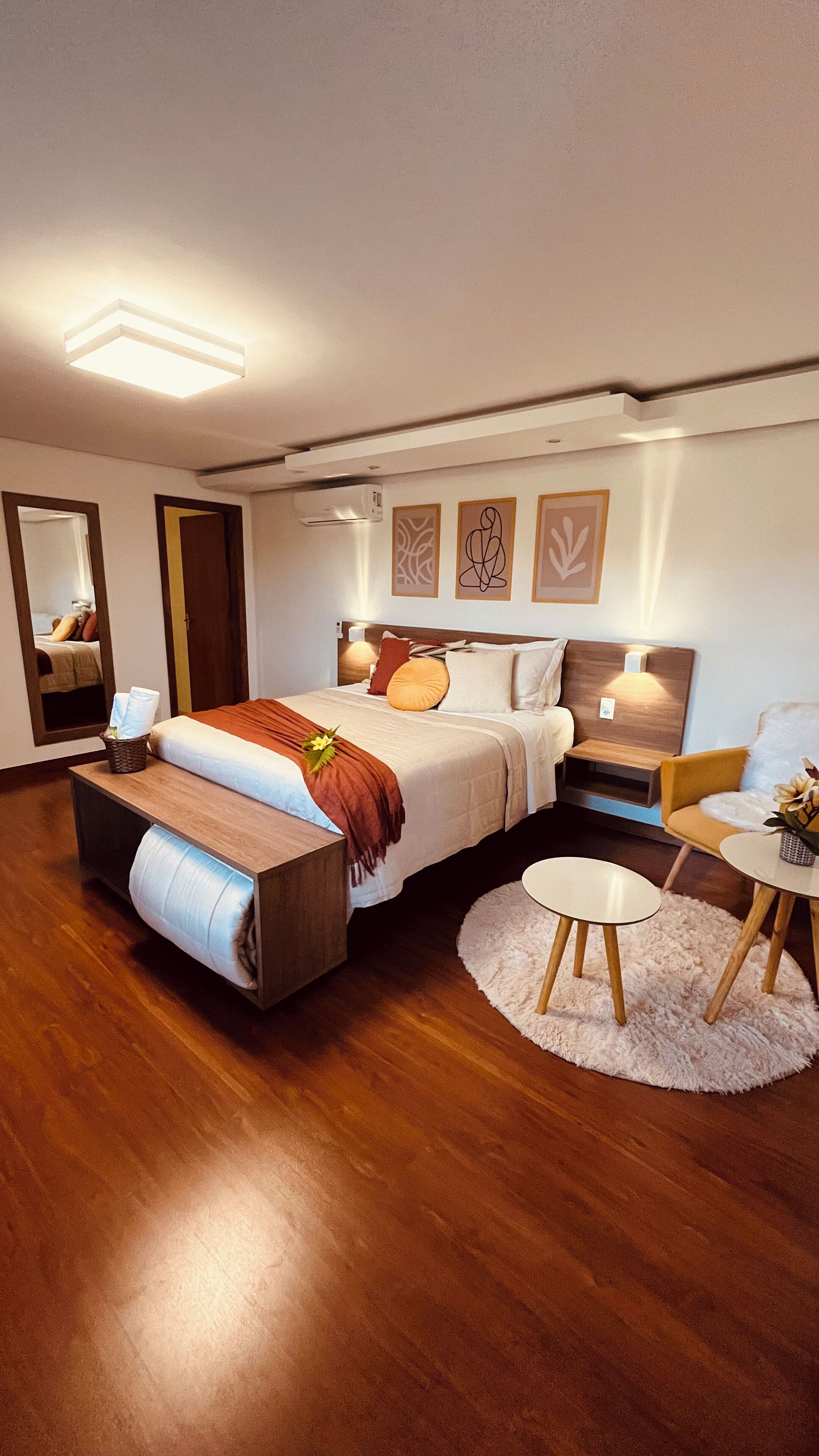 A modern hotel room with a large bed, bedside tables, a round table, and a mirror.