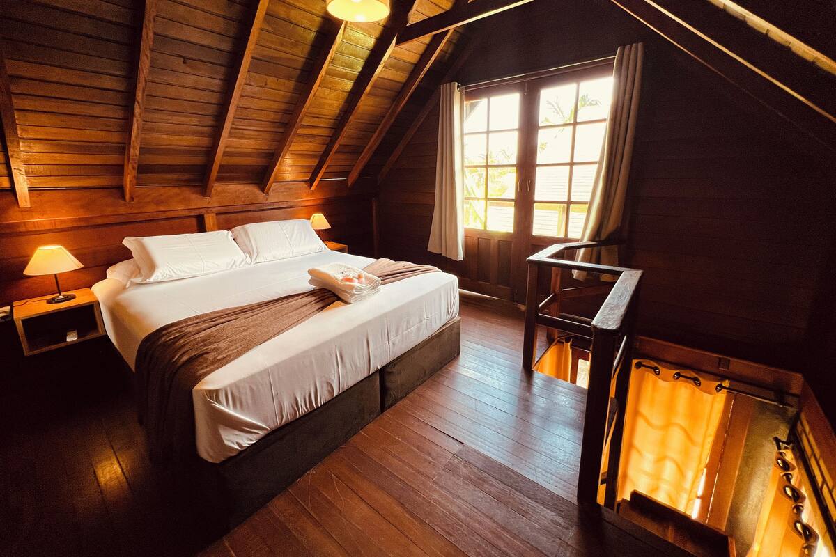 Une chambre à coucher chaleureuse, décorée dans un style rustique avec du bois, comprenant un grand lit, une table de chevet avec une lampe et une fenêtre avec des rideaux.