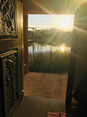 A view from inside a building to a body of water with a sunset in the background. - Pousada Xaxá (Palhoça)
