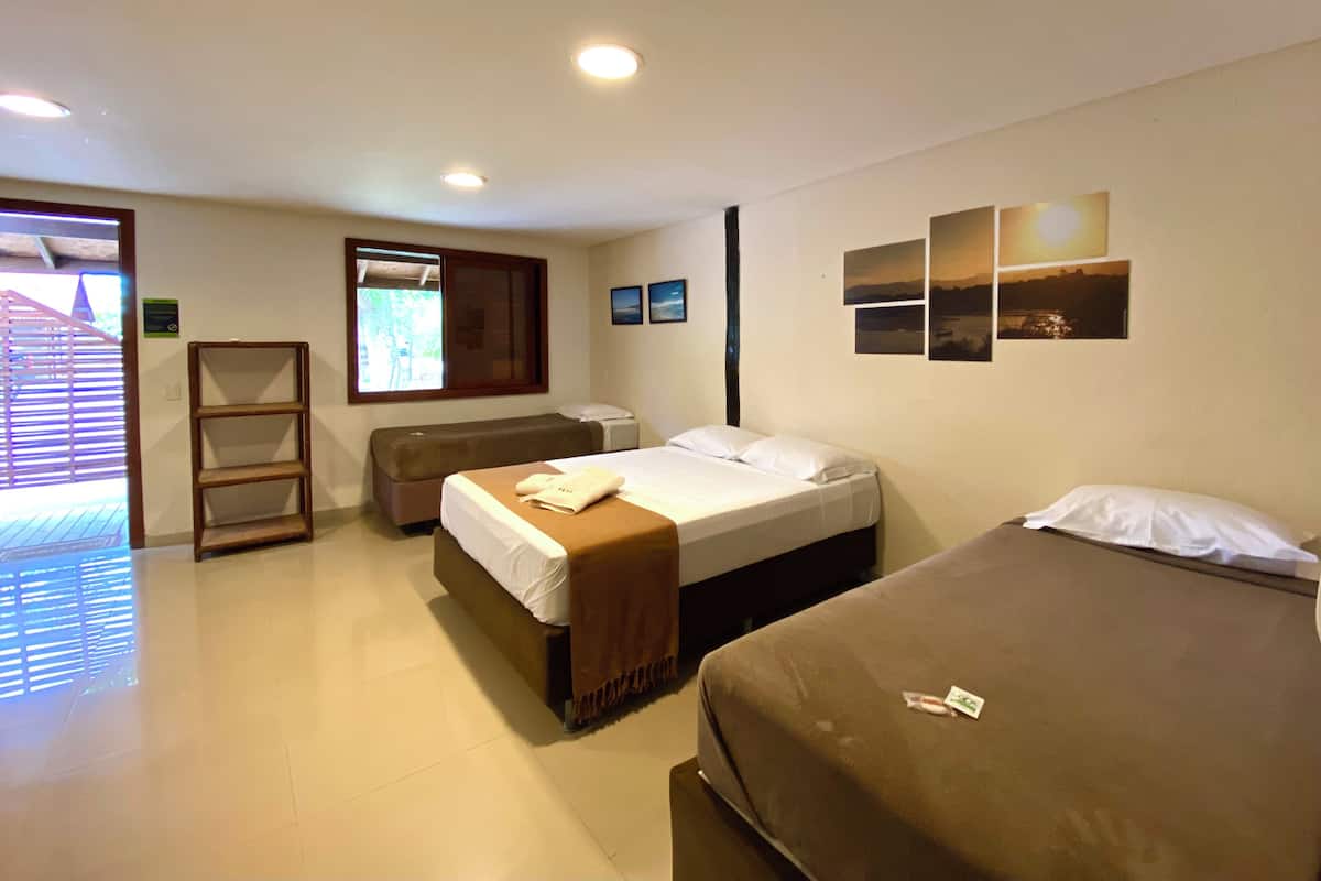 Une chambre d’hôtel avec deux lits, un petit coin salon, une fenêtre avec des stores et un mur orné de trois tableaux.