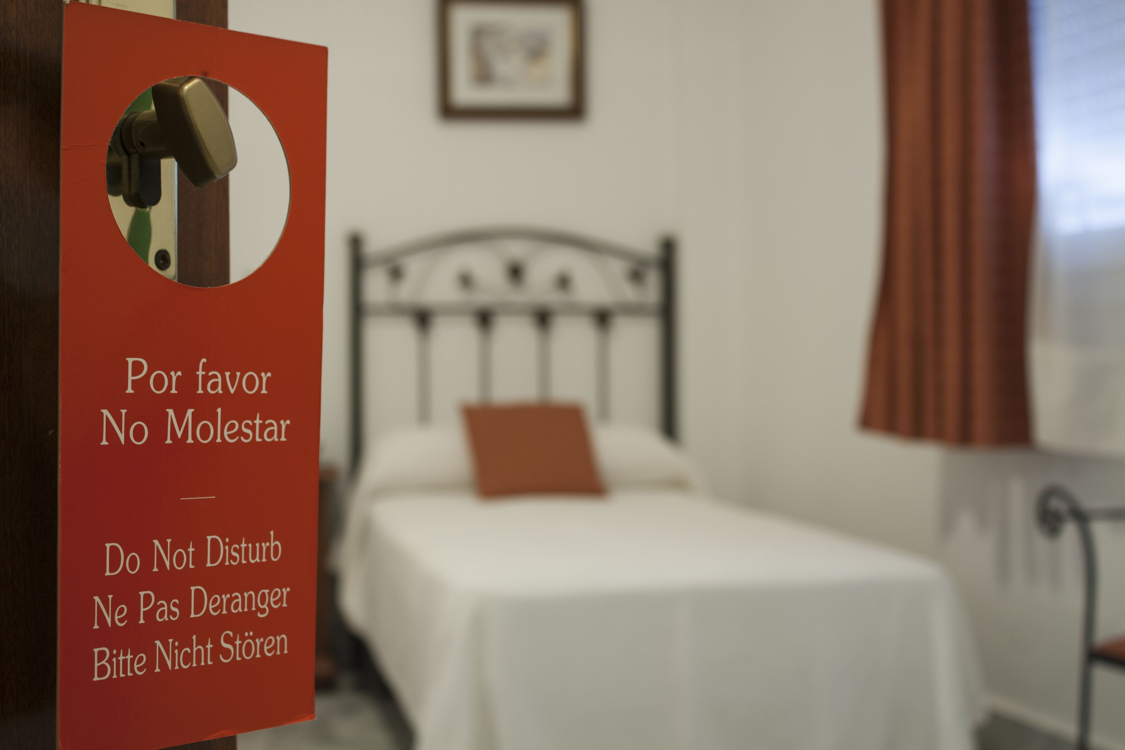 Una habitación de hotel con una cama, un cartel rojo con instrucciones en varios idiomas y una ventana con cortinas.