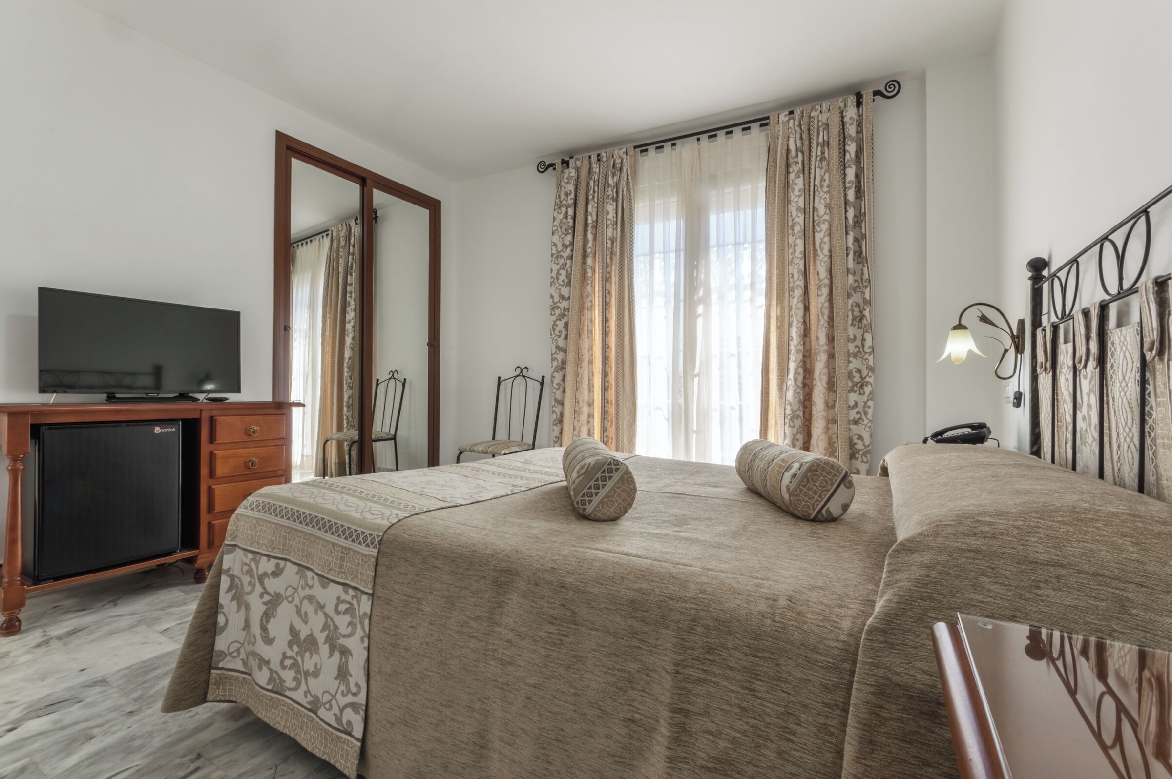 A hotel room with a bed, a desk with a television, and a wardrobe.