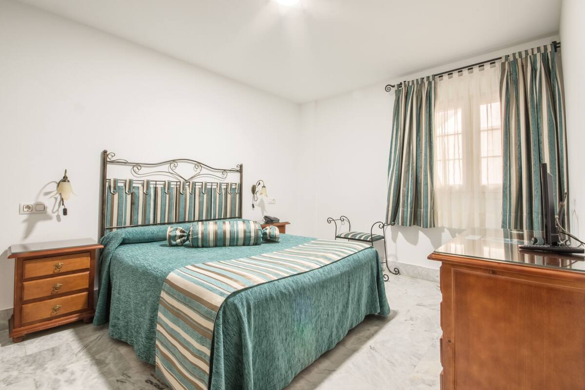 A bedroom with a bed, nightstands, a dresser, and a window with curtains.