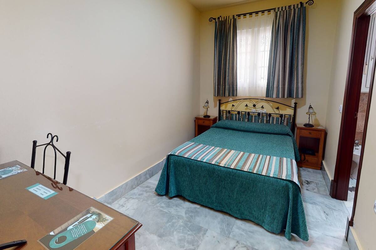 A bedroom with a bed, a nightstand, a table, and a chair.