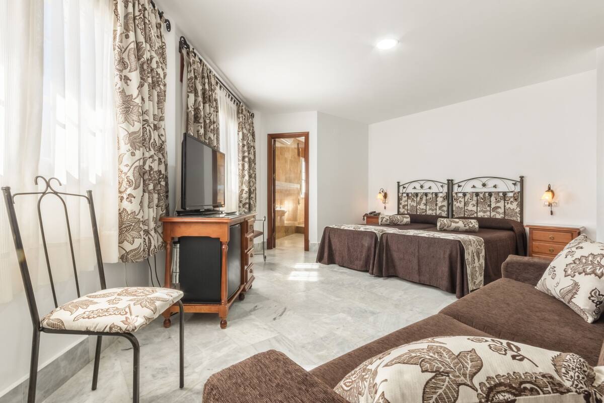 A hotel room with a bed, a desk, a chair, a TV, and a wardrobe.