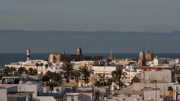 A coastal cityscape with historic buildings, a prominent lighthouse, and a view of the sea.