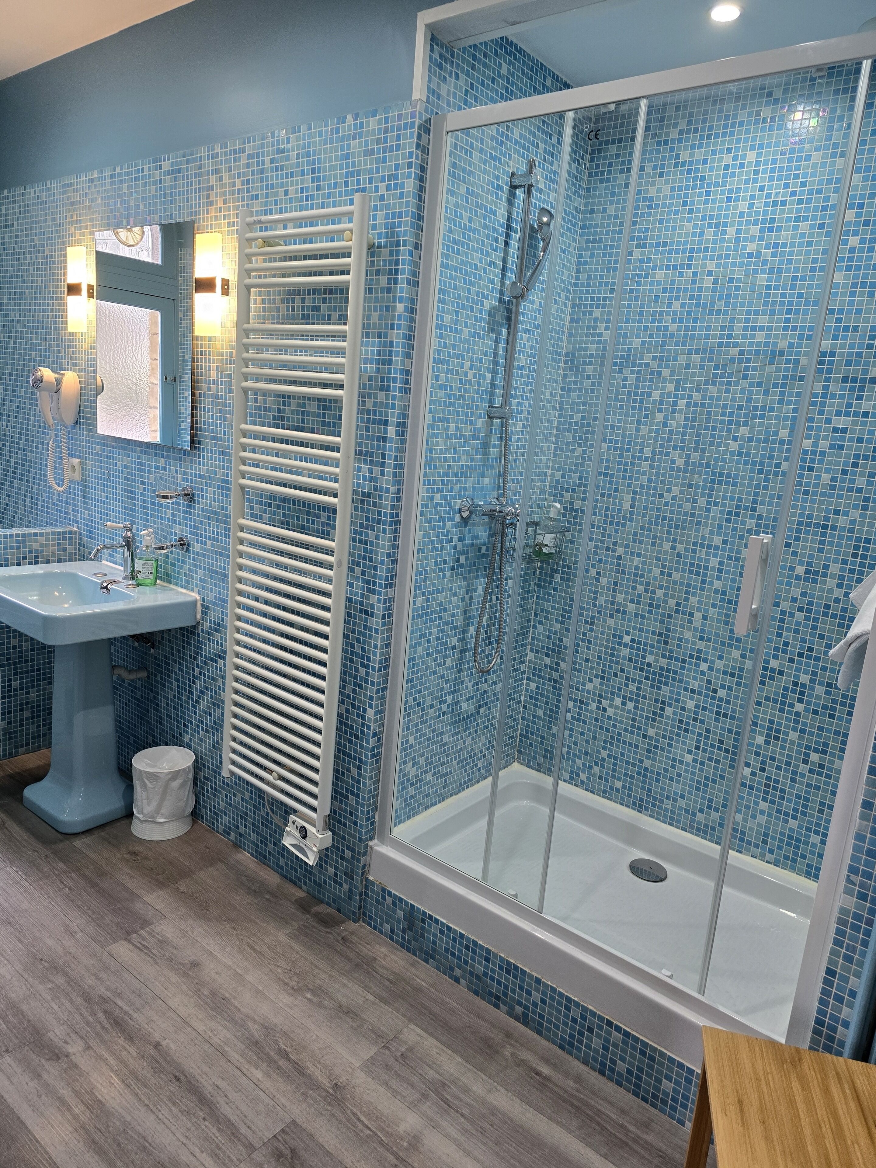 A bathroom with a blue-tiled shower, a pedestal sink, and a towel rack.