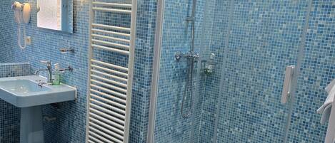 A bathroom with a blue-tiled shower, a pedestal sink, and a towel rack.