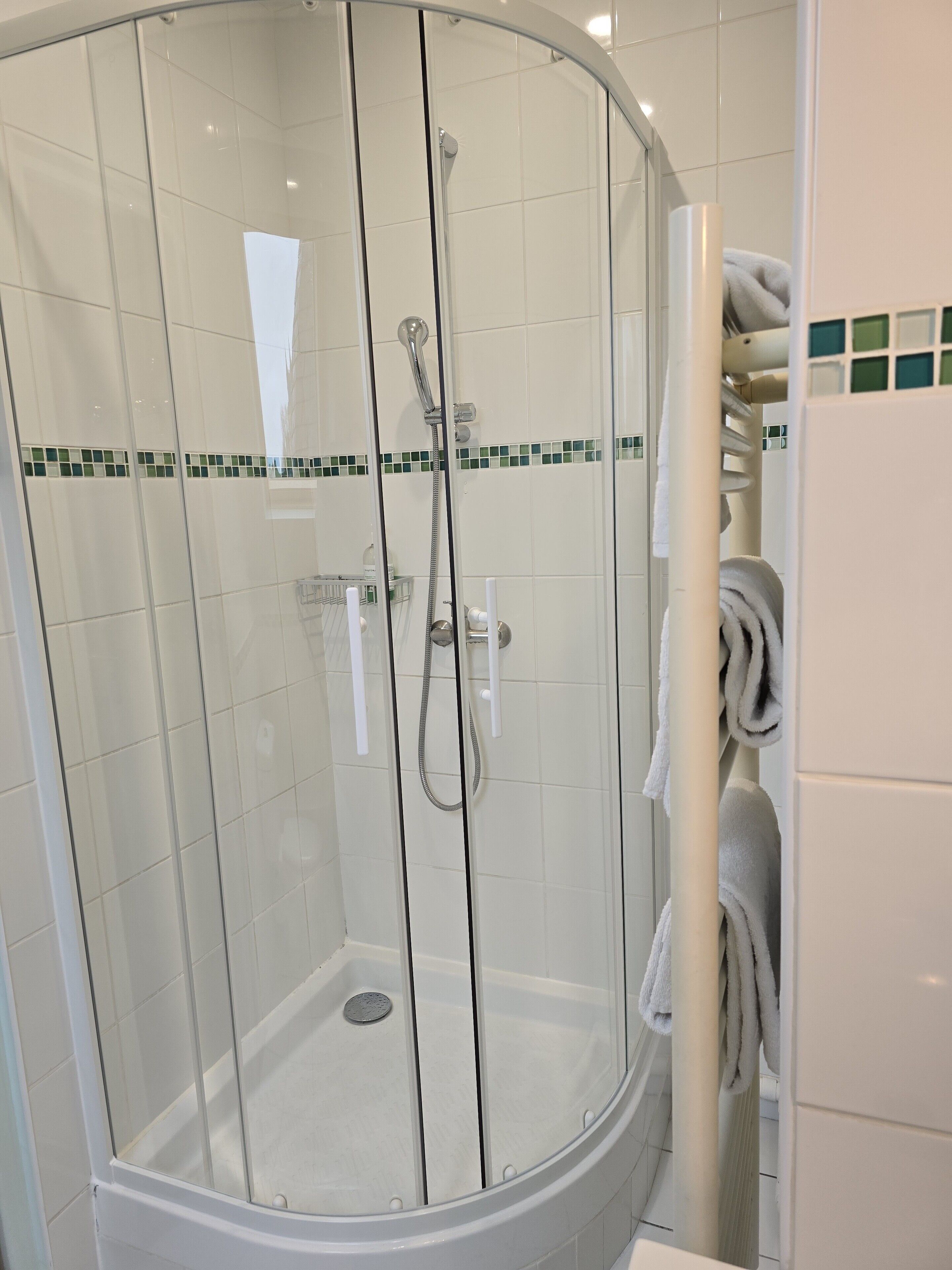 Een glazen douchecabine met een witte betegelde wand, een glazen deur en een klein plankje met toiletartikelen.
