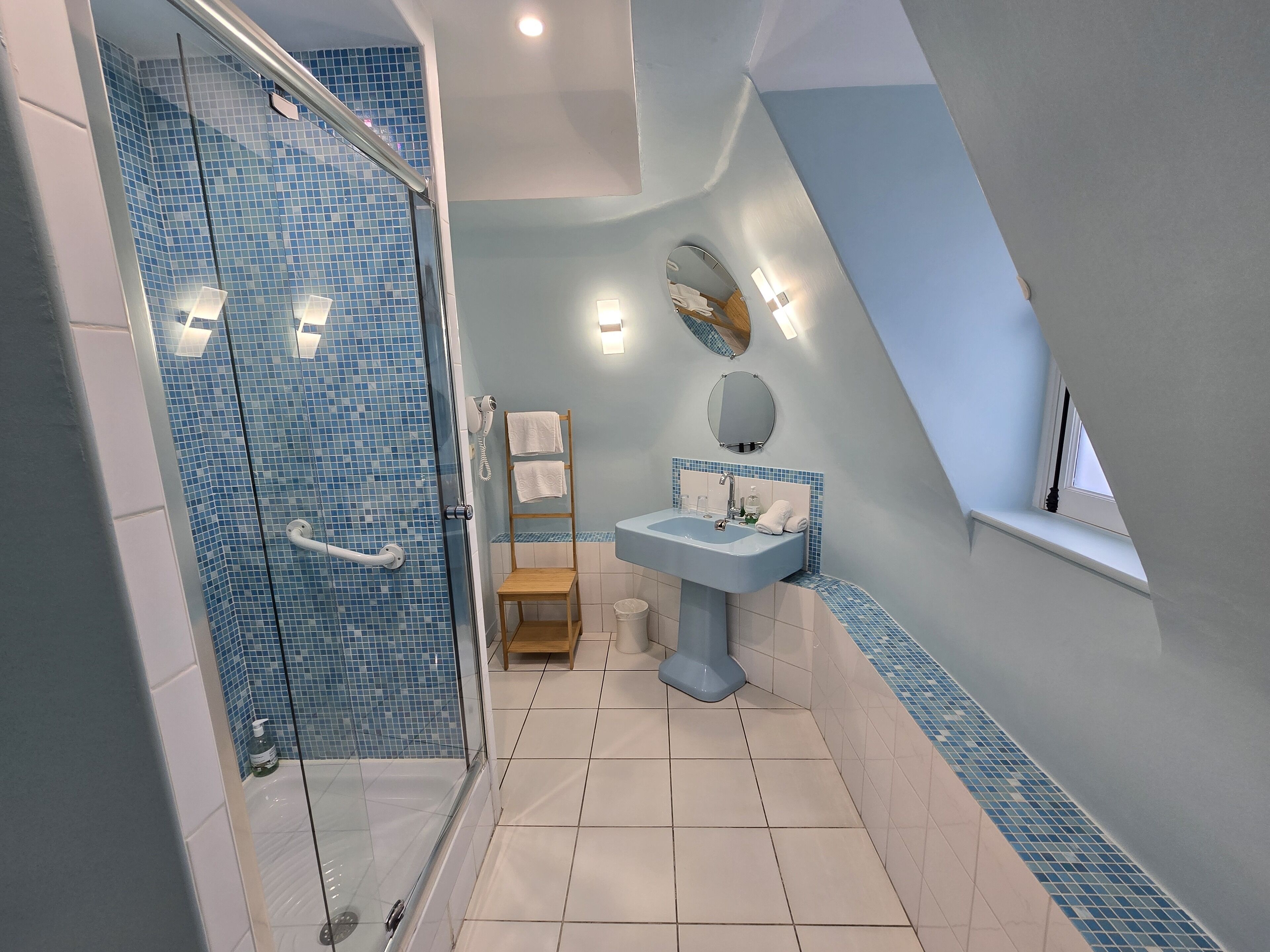 A bathroom with a glass shower enclosure, a sink with a mirror, and a window.