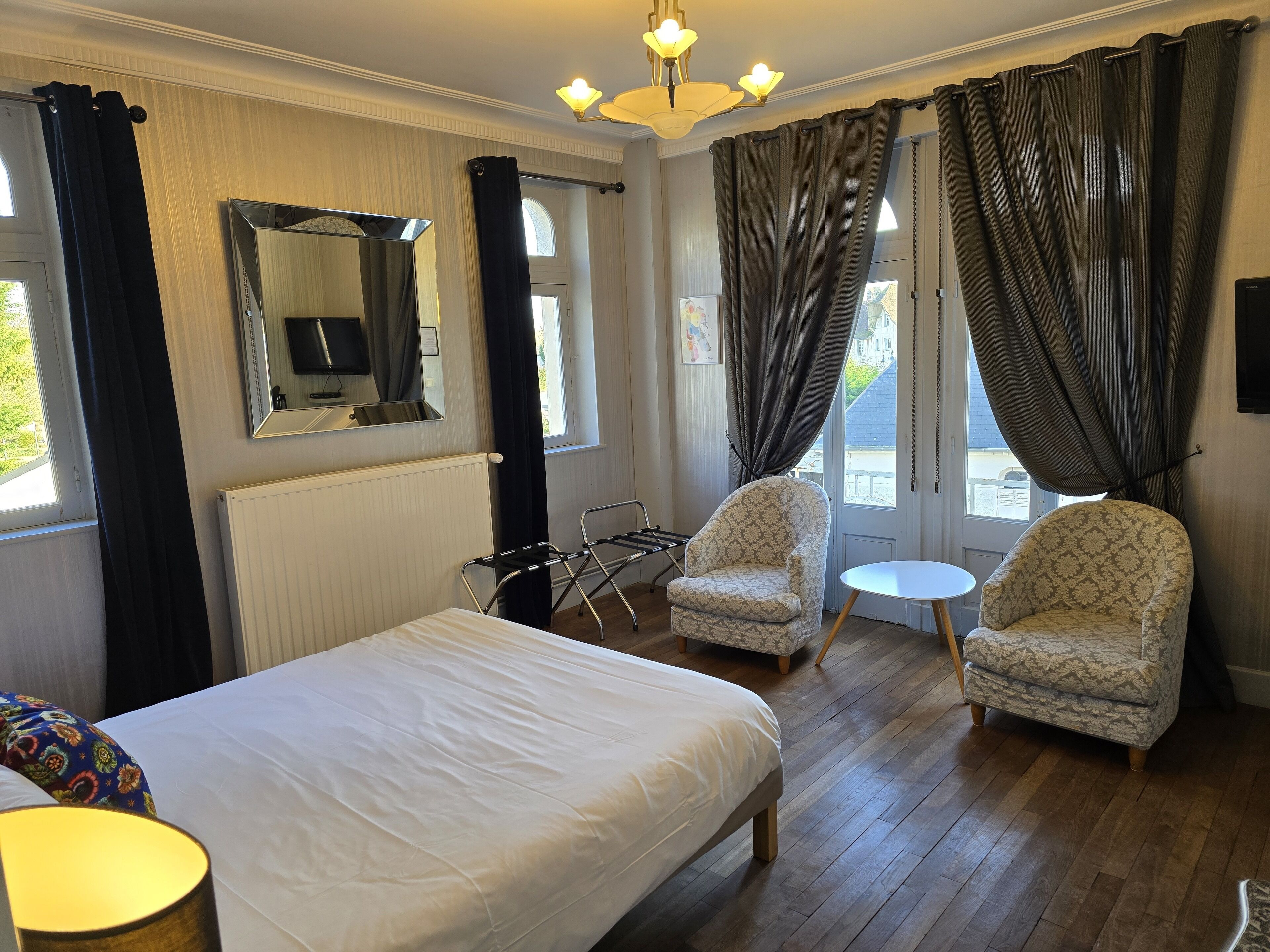 Habitación de hotel con una cama grande, dos sillones, una mesita, un espejo y vistas al exterior.