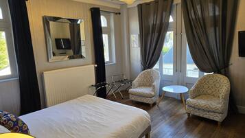 Habitación de hotel con una cama grande, dos sillones, una mesita, un espejo y vistas al exterior.
