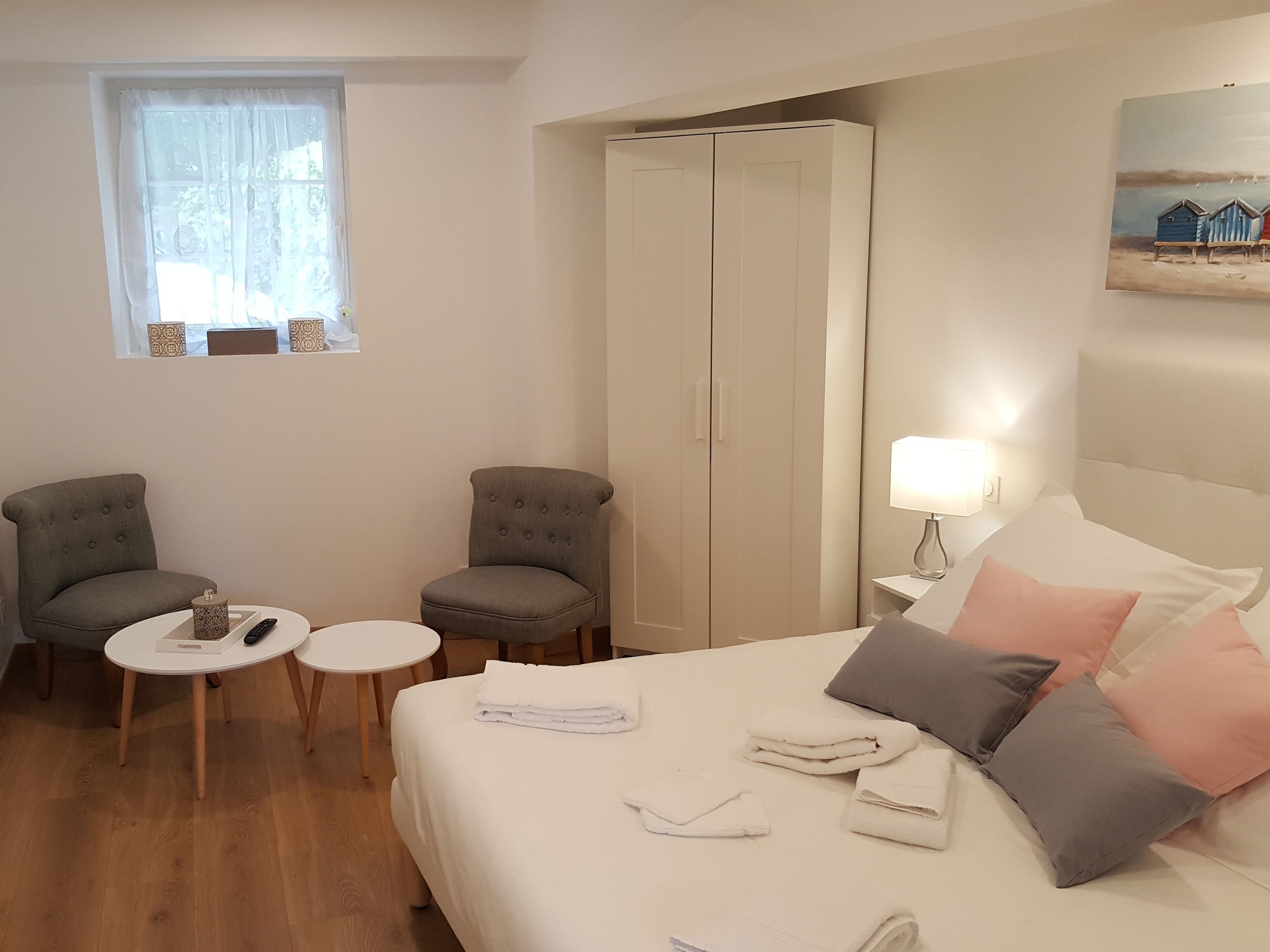 A hotel room with a bed, two armchairs, a small table, a wardrobe, and a window with curtains.