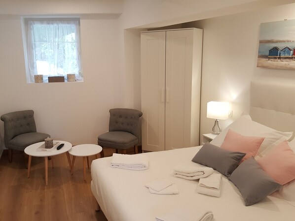 A hotel room with a bed, two armchairs, a small table, a wardrobe, and a window with curtains.