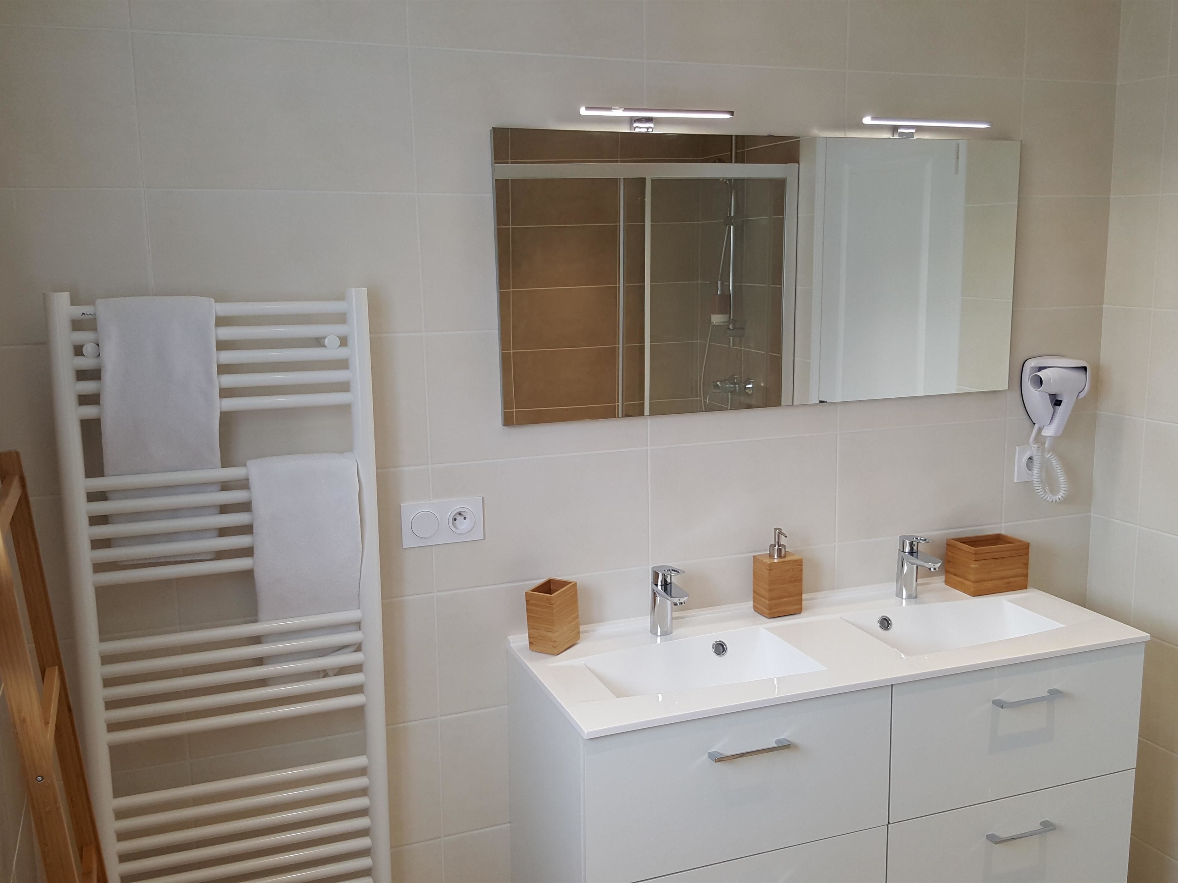 A modern bathroom with a white vanity, two sinks, a mirror, and a towel rack.