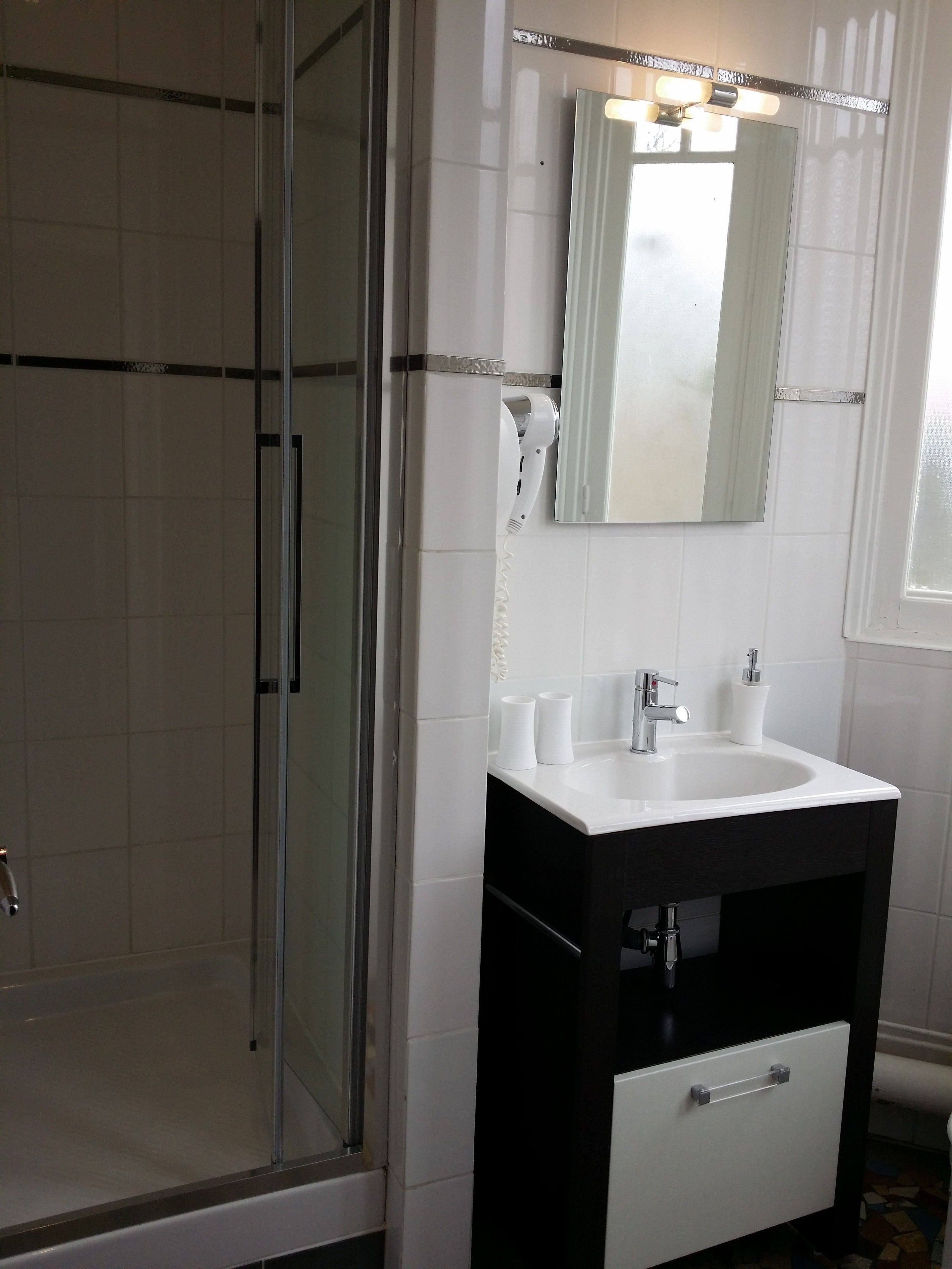 A bathroom with a glass shower enclosure, a white sink with a black cabinet, and a mirror above the sink.