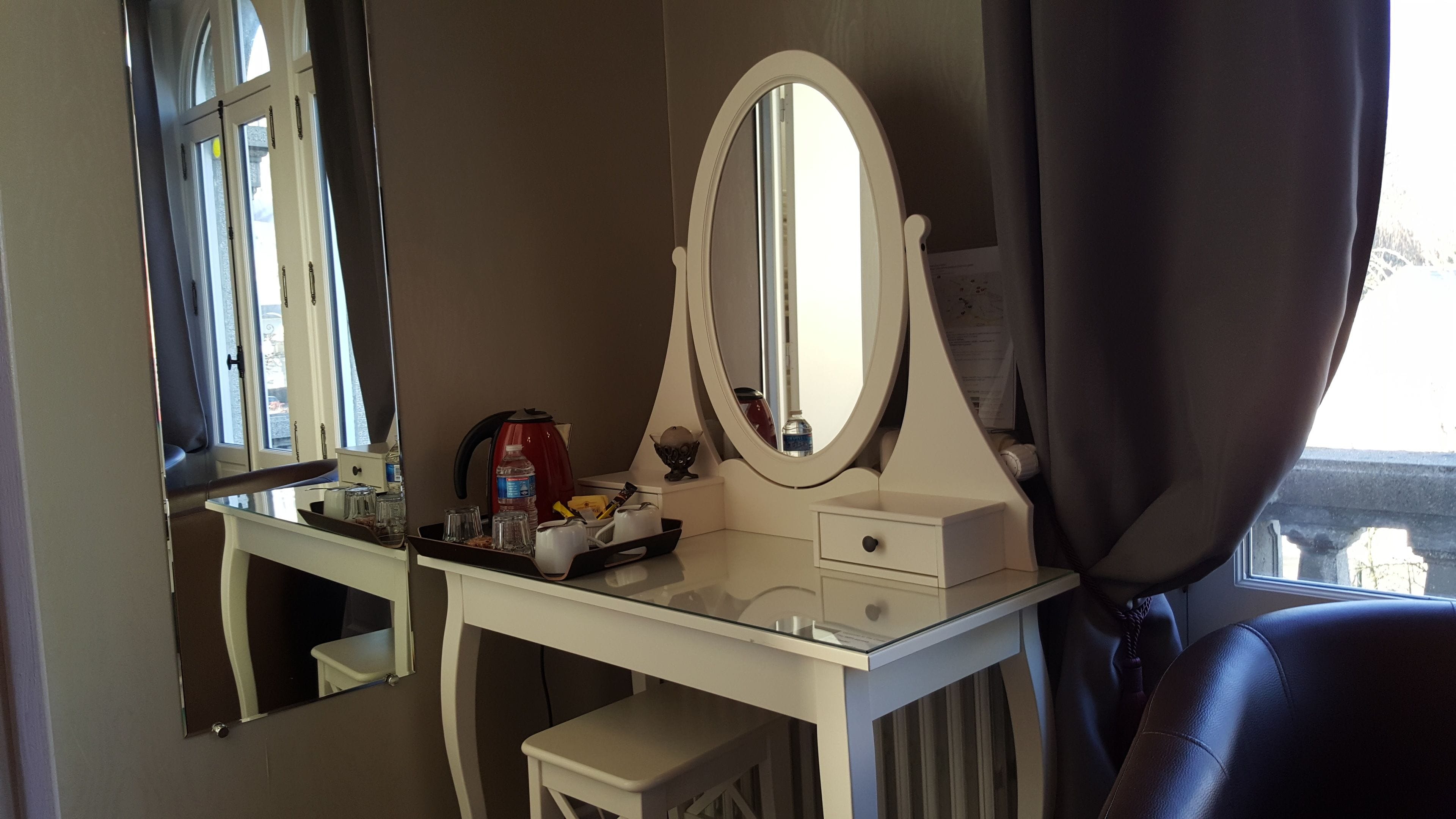 A room with a white vanity, a large mirror, a window with curtains, and a view of a bridge.