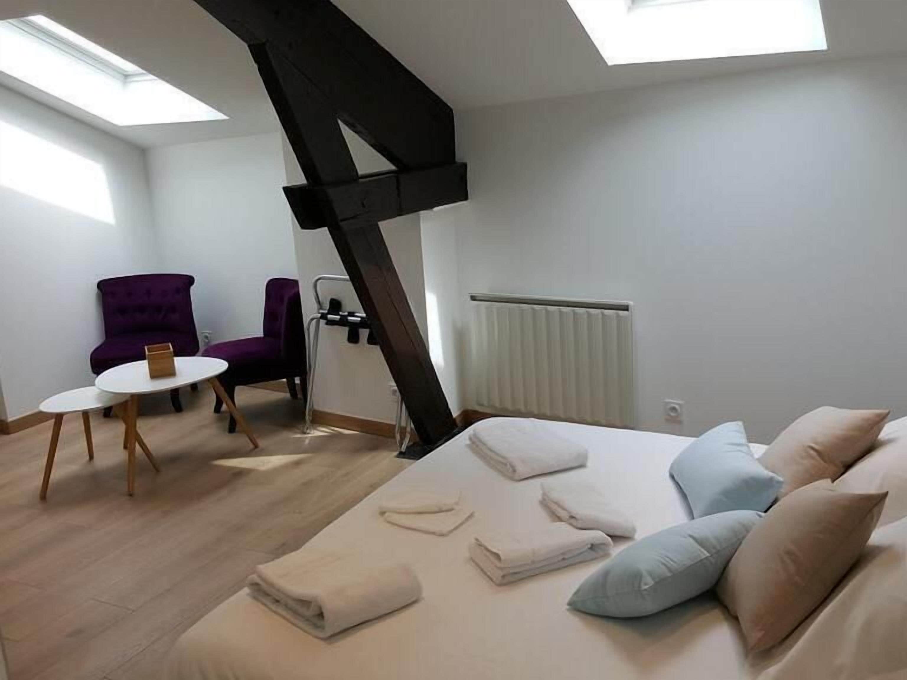 Une chambre moderne avec un puits de lumière, un lit avec des oreillers, une chaise, une petite table et un radiateur.