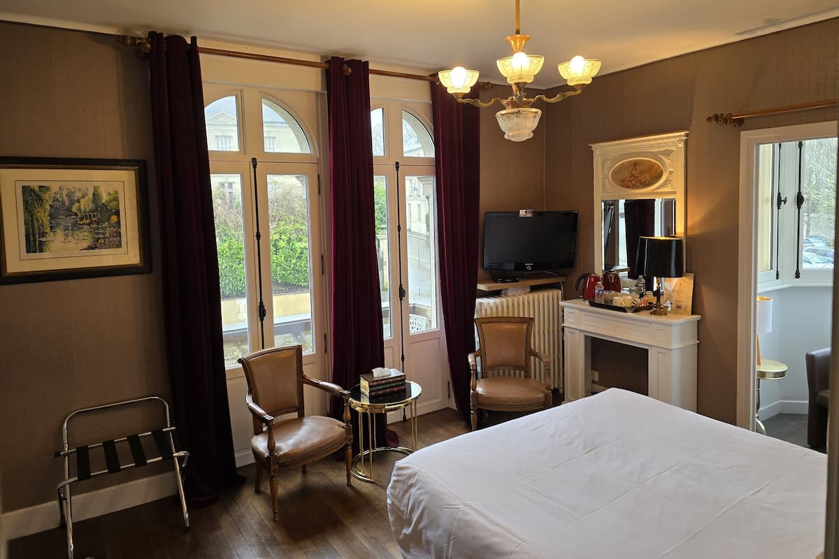 A hotel room with a bed, a desk with a television, a chair, a small table, and a radiator.