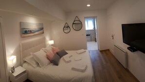 Habitación de hotel con cama, televisor, un cuadro y baño visible a través de una puerta abierta.