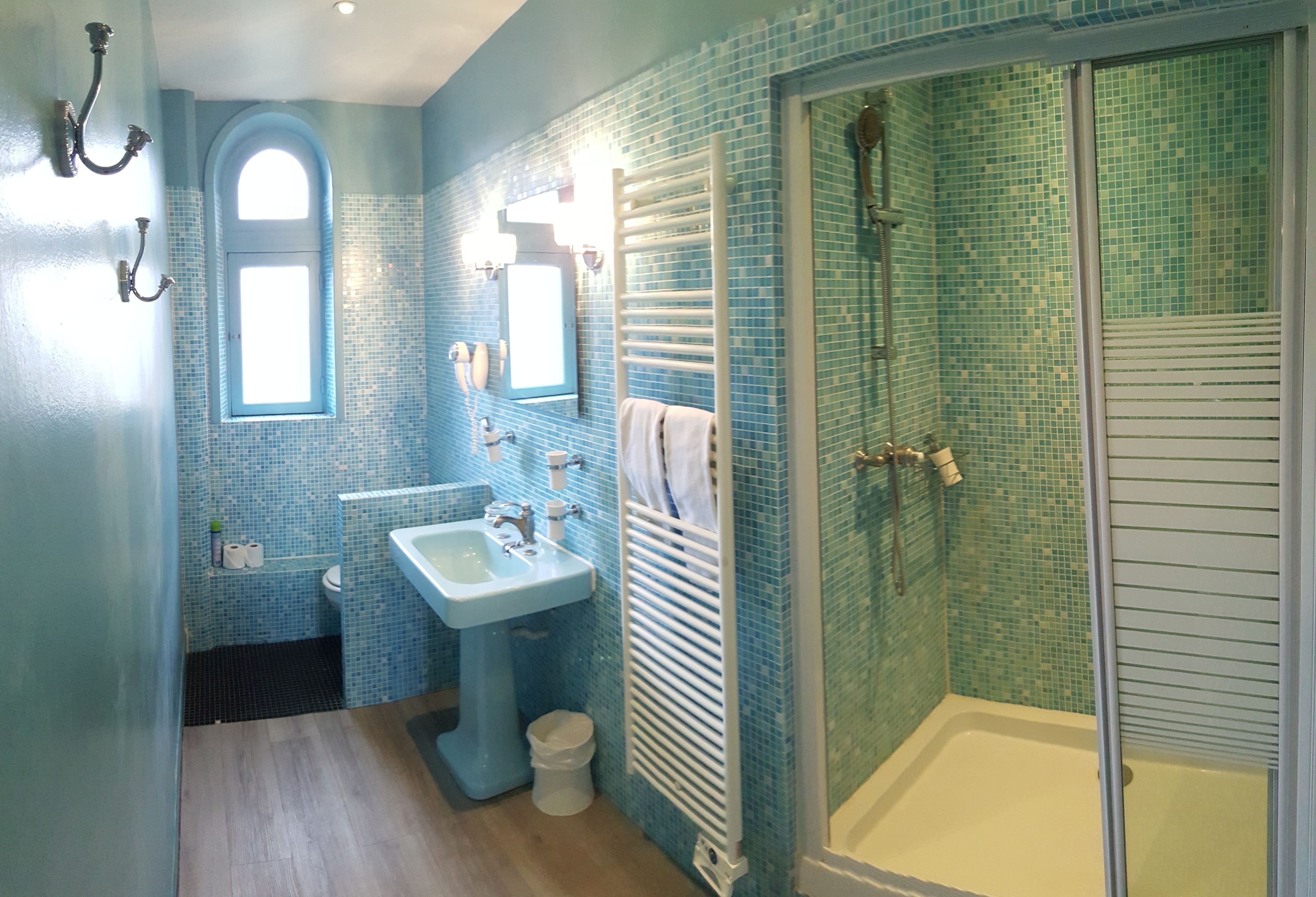 Een badkamer met een blauwe betegelde wand, een wastafel, een spiegel, een handdoekhouder en een douchegedeelte.