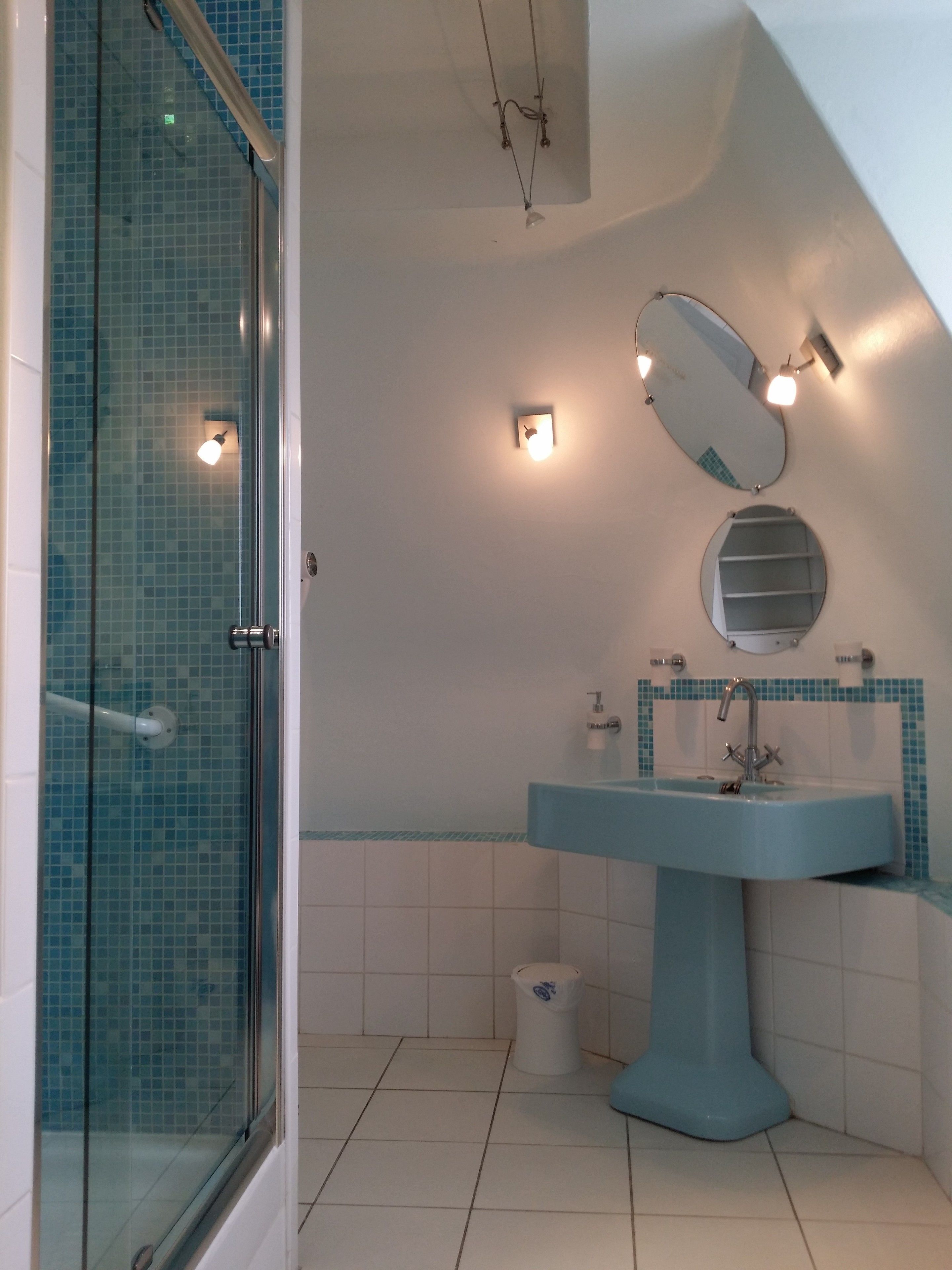A bathroom with a glass shower enclosure, a blue sink, a mirror, and a toilet.