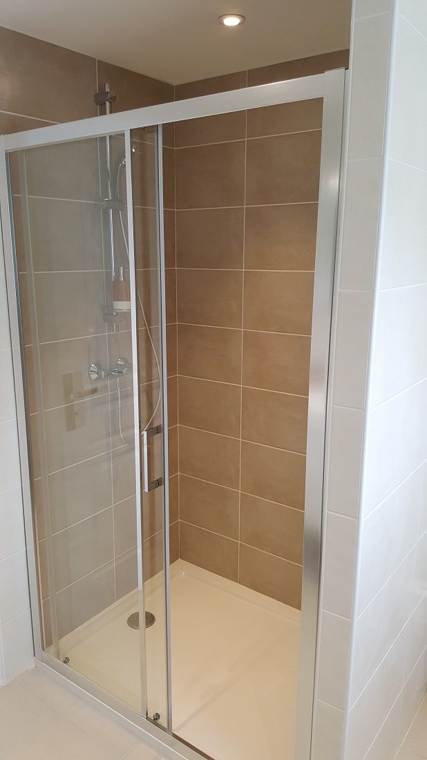 A glass-enclosed shower stall with a white floor and brown tiles on the walls.
