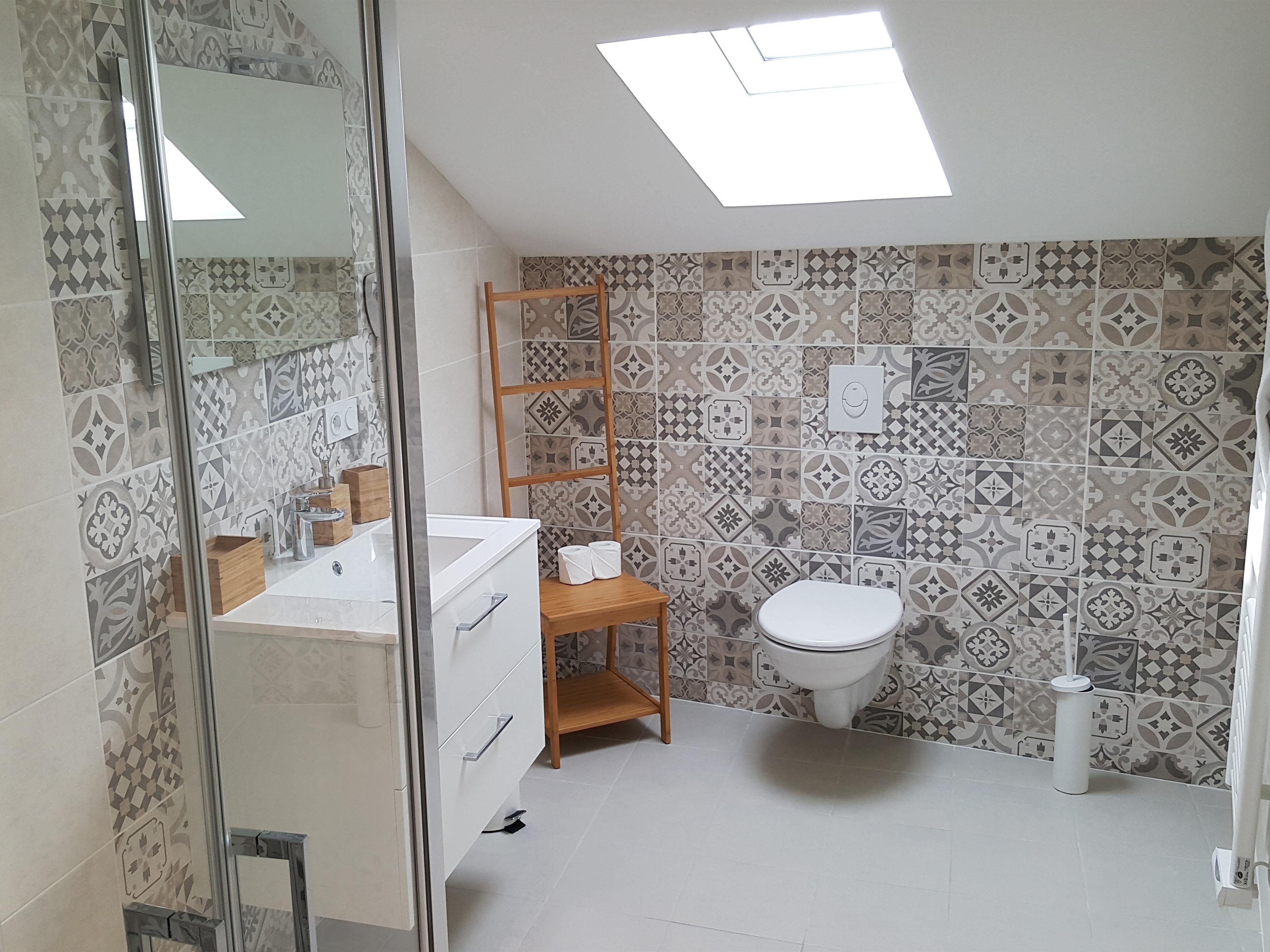 A bathroom with patterned tiles, a white toilet, a wooden shelf, and a skylight.