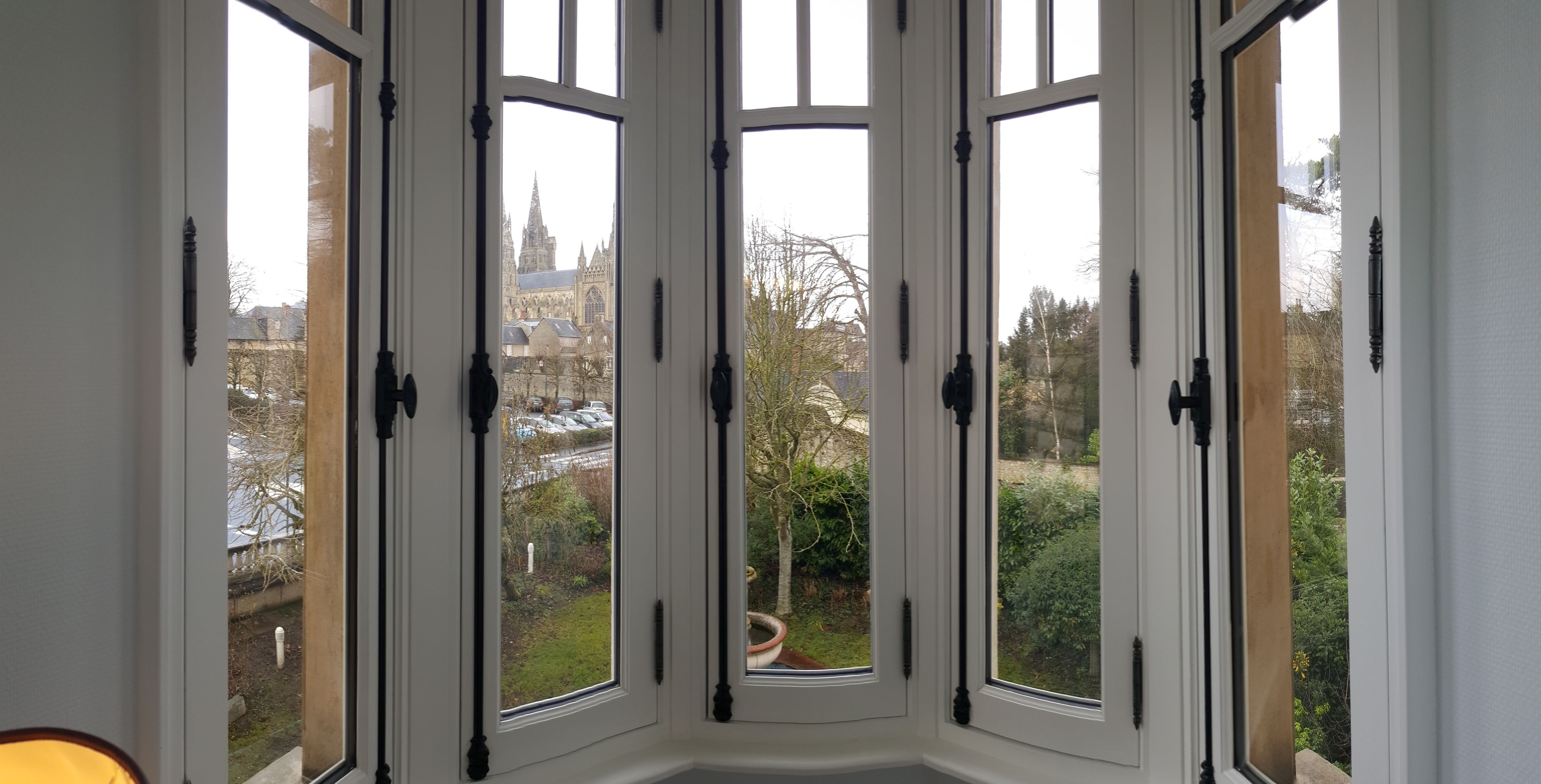 A bay window with multiple panes, offering a view of a historic building and a garden.