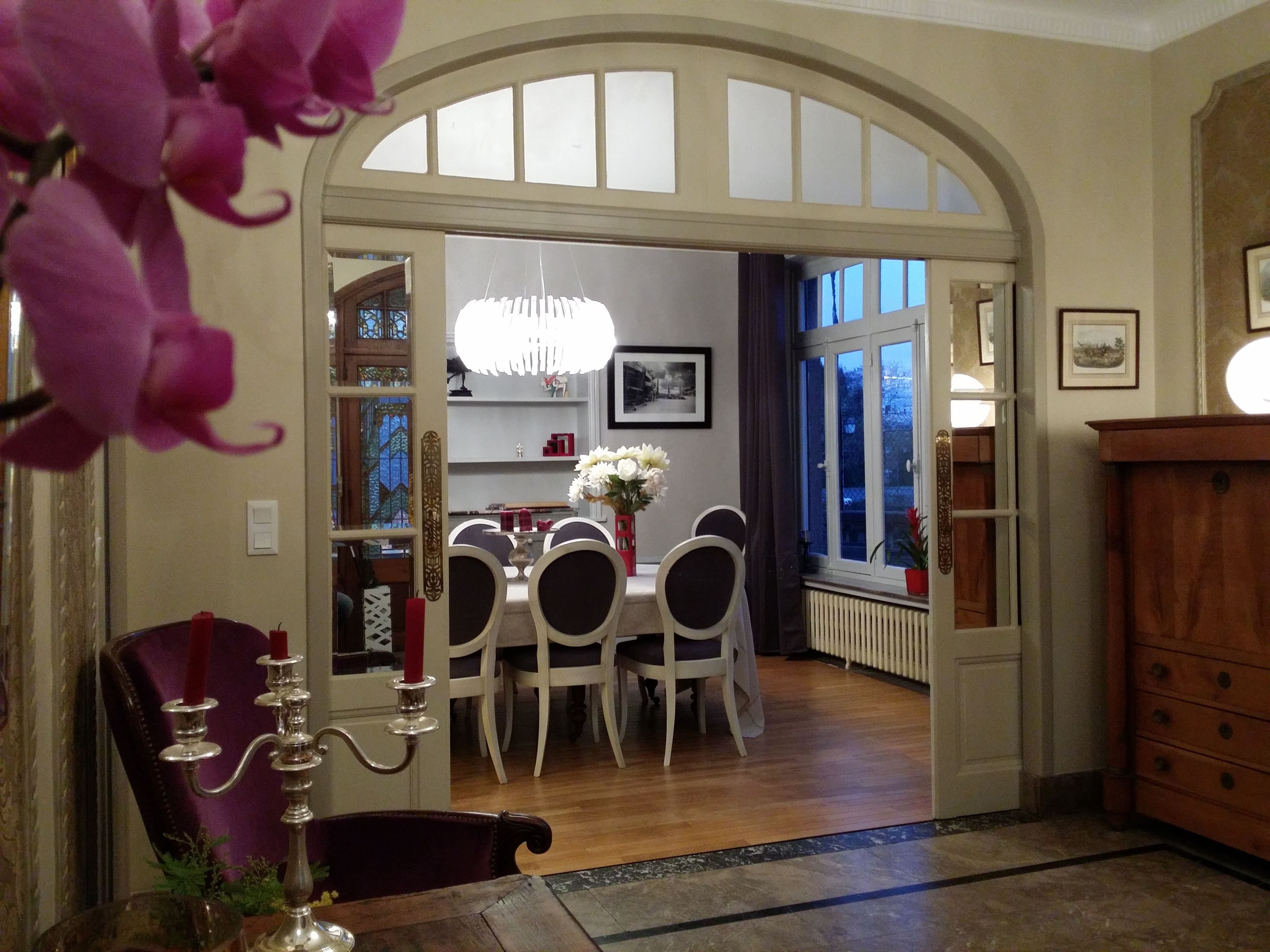 A dining area with a chandelier, white chairs, and a table.