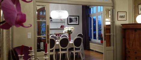 A dining area with a chandelier, white chairs, and a table.