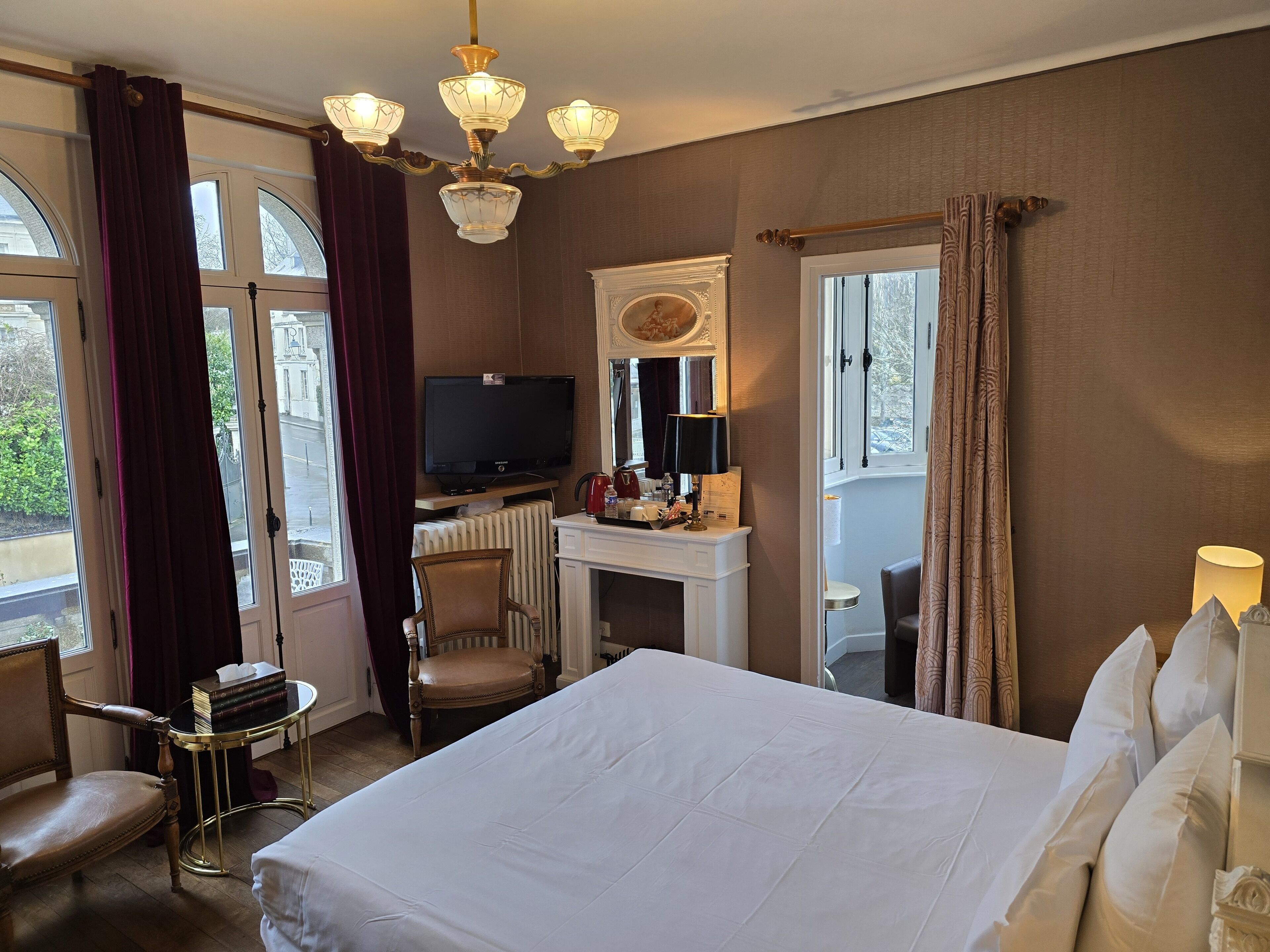 A hotel room with a large bed, a desk with a television, a chair, and a view of the outdoors.
