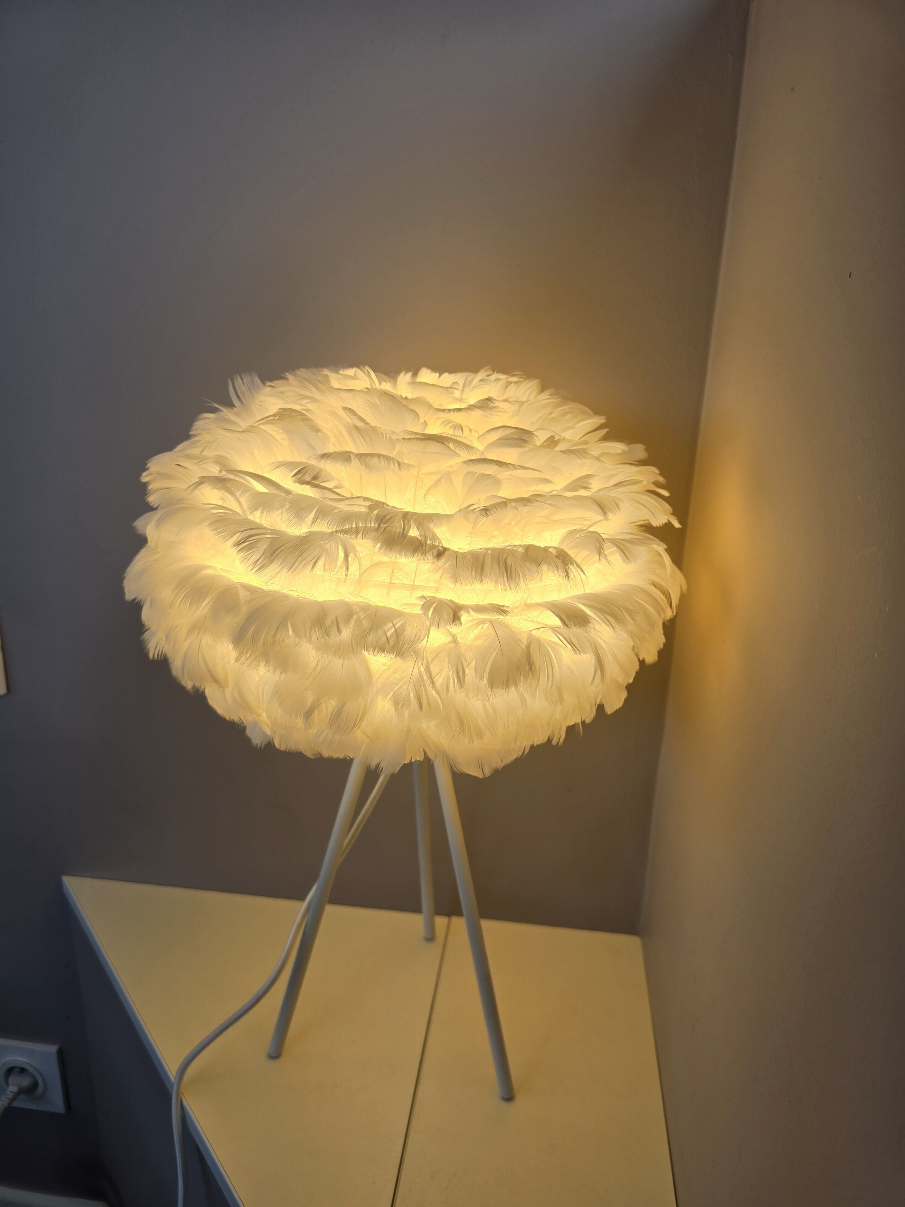 Een ronde tafel met een lamp met veren op een witte standaard.